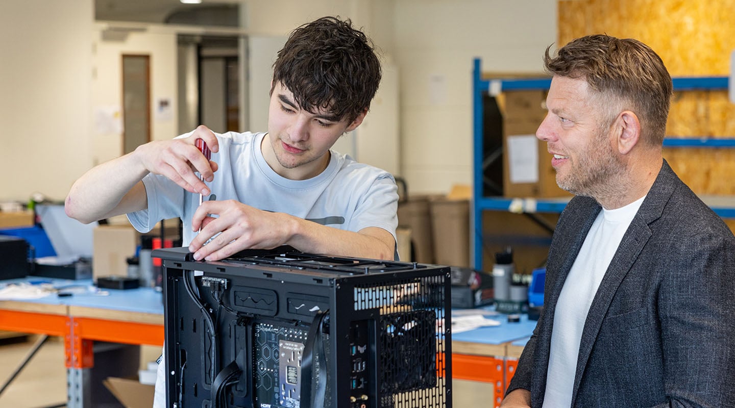 Een jonge Azerty-medewerker bouwt een pc terwijl een collega lachend meekijkt