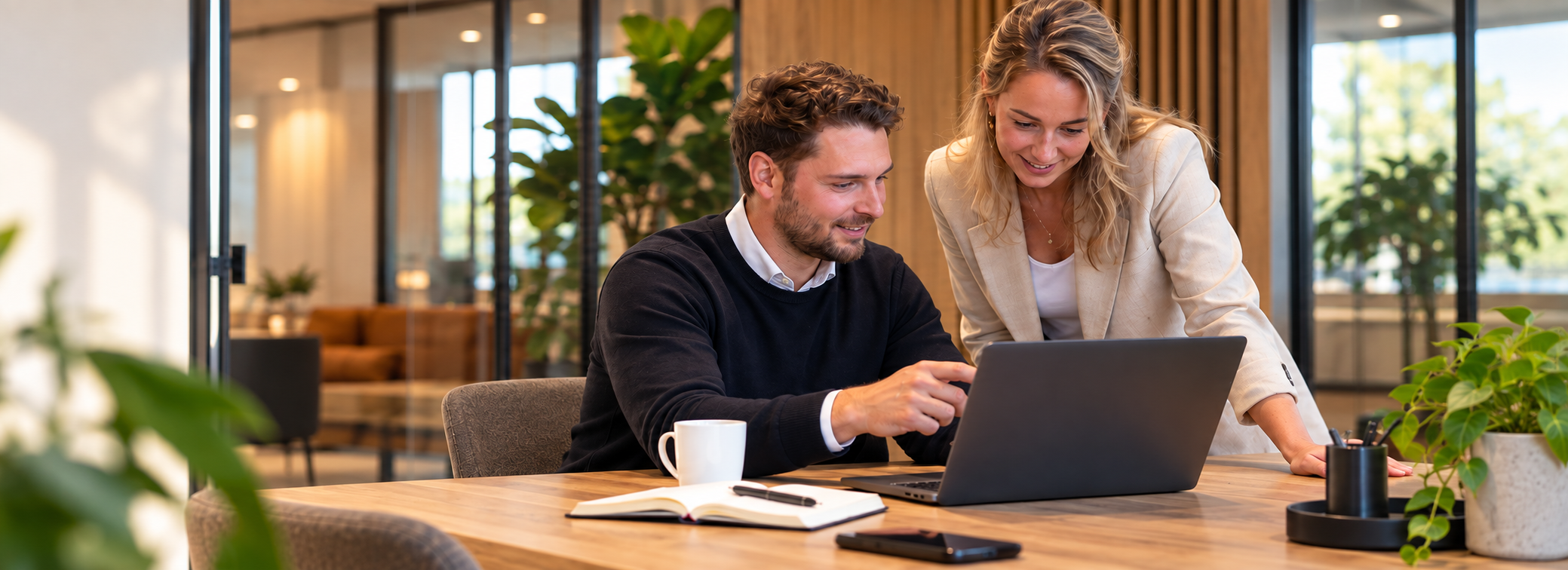 Twee collega's bekijken samen een laptop in een kantooromgeving
