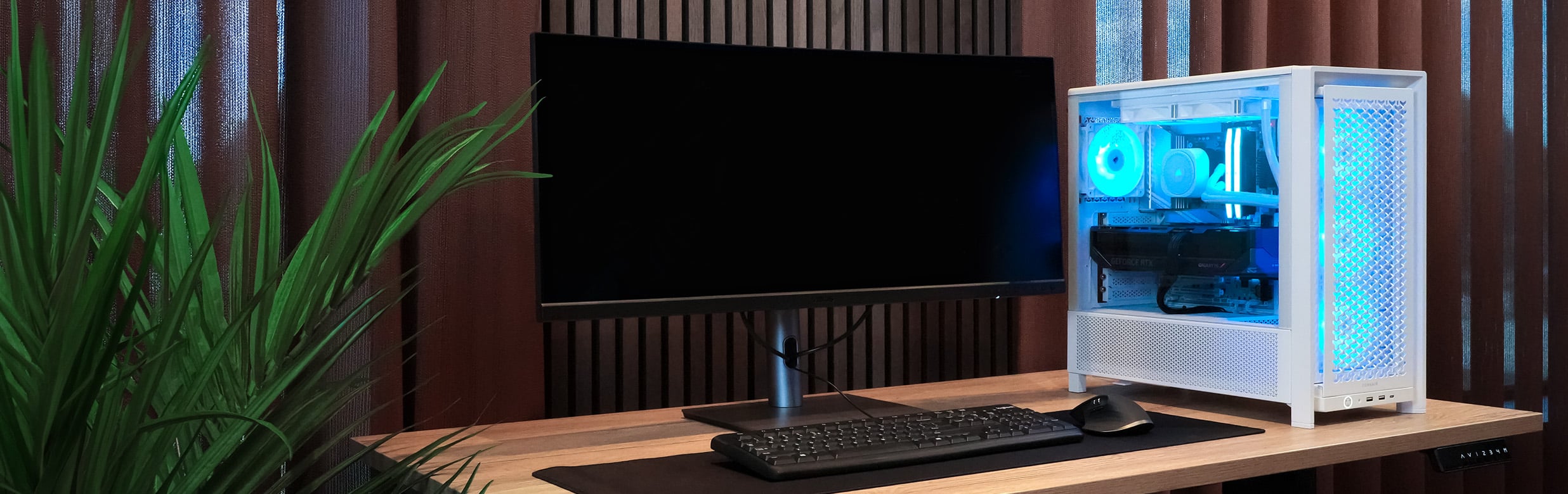 Witte Xenith pc met blauwe RGB-verlichting op een bureau naast een ultrawide monitor